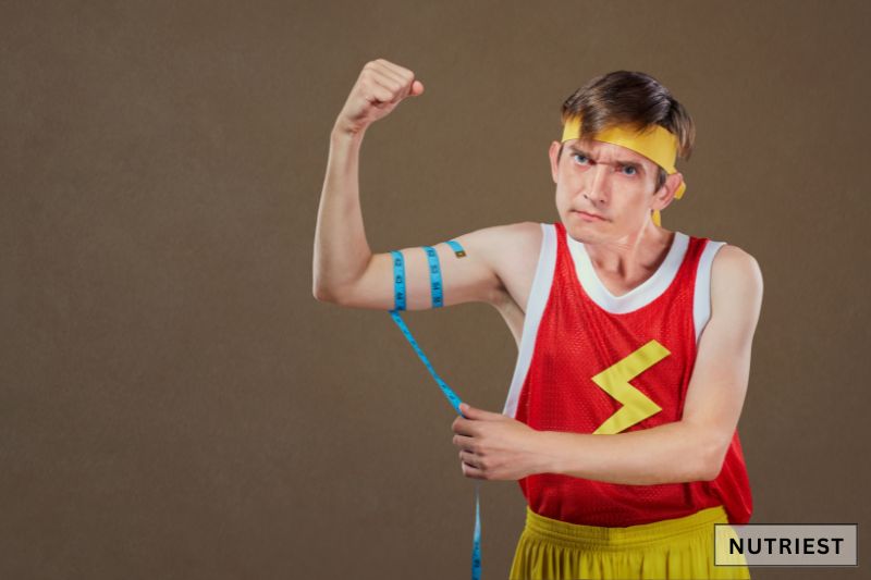 A humorous fitness pose, flexing his bicep while measuring it with a tape hinting at the desire to build strength and muscle