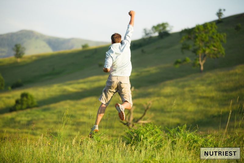 A man leaping joyfully in an open green field symbolizing energy that indicate the potential benefits of increased testosterone levels