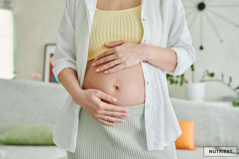 Pregnant woman cradling belly at home, reflecting can you take collagen while pregnant
