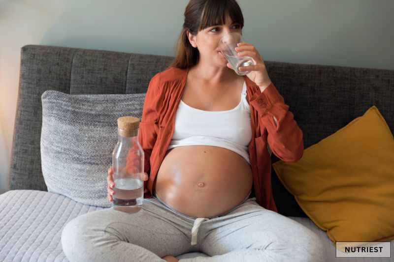 Pregnant woman drinking water on bed, symbolising can you take collagen while pregnant
