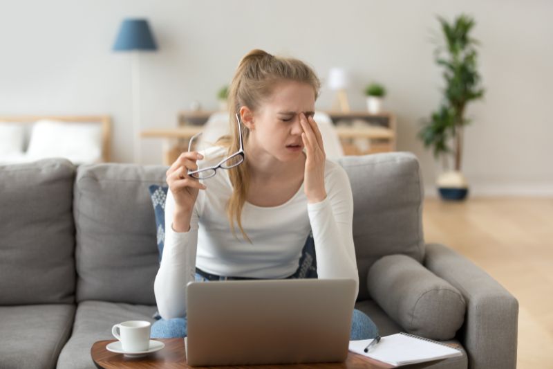 Woman rubbing tired eyes, possible signs of low iron eyes while working on laptop